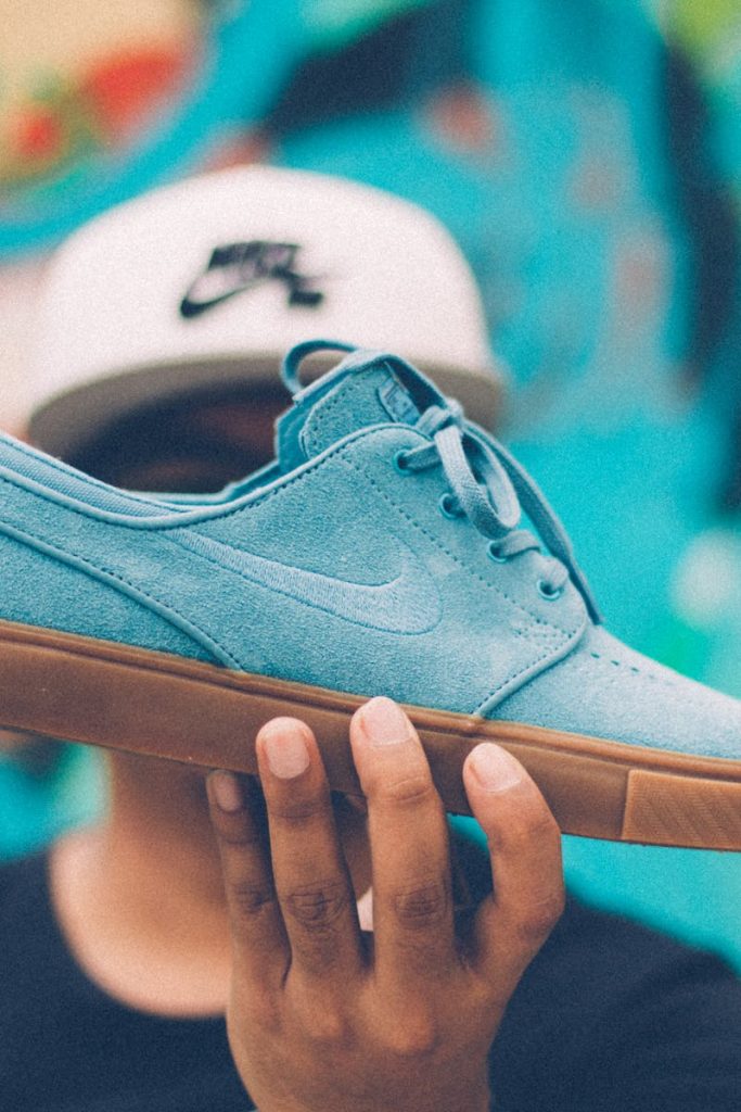 Close-up of a blue skate shoe held by a young adult against a colorful background.