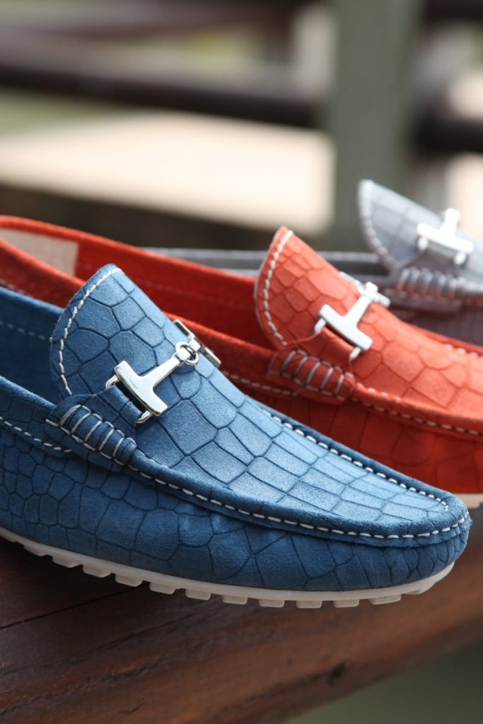 Fashionable leather loafers in various colors displayed on a wooden railing outdoors.